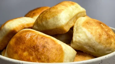 Zlatno zapečeni jogurt jastučići naslagani u bijeloj zdjeli — mekano, prhko tijesto rumene korice.