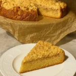 Jedan komad Crumble kolača s jabukama na bijelom tanjiru, prikazan uredno u krupnom kadru, sa hrskavim posipom