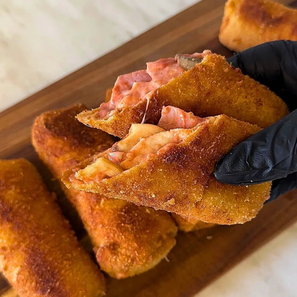 Pizza punjene pohane palačinke s hrskavom koricom i sočnim punjenjem od sira, šunke i umaka za pizzu, servirane na drvenoj dasci