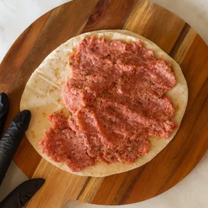 Ravnomjerno razmazivanje začinjene smjese od mljevenog mesa po tortilji na drvenoj dasci, priprema za rezanje i pečenje