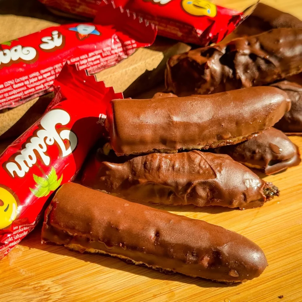 Čokoladne domaće krem bananice složene na drvenoj podlozi uz pakiranja Jaffa bananica