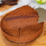 Komad čokoladne mousse torte na metalnoj lopatici, s bogatim čokoladnim slojem i finim posipom od kakaa