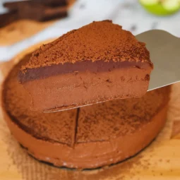Komad čokoladne mousse torte na metalnoj lopatici, s bogatim čokoladnim slojem i finim posipom od kakaa
