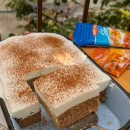 Sočan kremasti kolač sa cimetom u plavom kalupu, prekriven šlagom i posut cimetom, s izrezanim kockama spremnim za serviranje