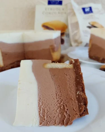 Presjek cheesecakea s tri sloja čokolade i hrskavom podlogom od keksa, prikazan izbliza na bijelom tanjuru.